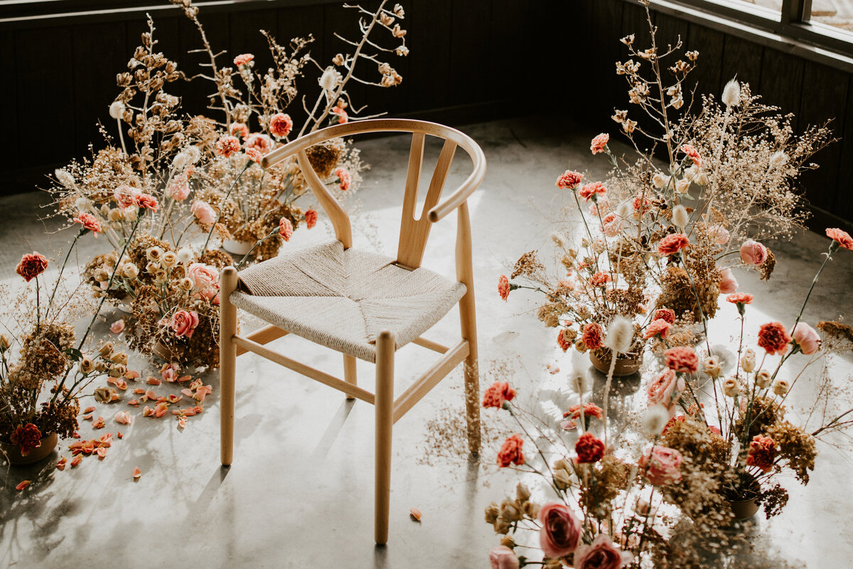 Light-colored wishbone chair surrounded by an assortment of blush flower arrangements.