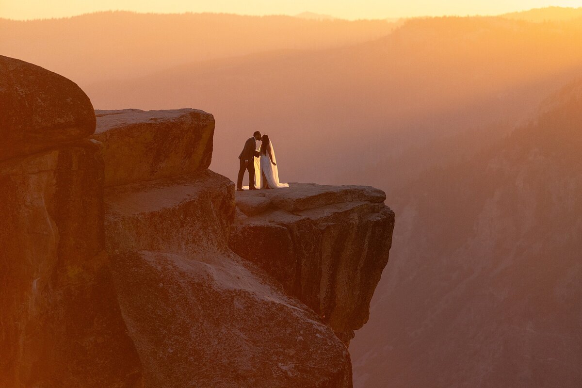 groom kisses bride on a cliffside in yosemite