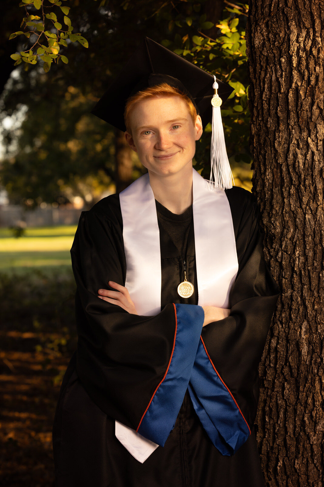 college-graduate-leaning-on-tree-oin-cap-and-gown