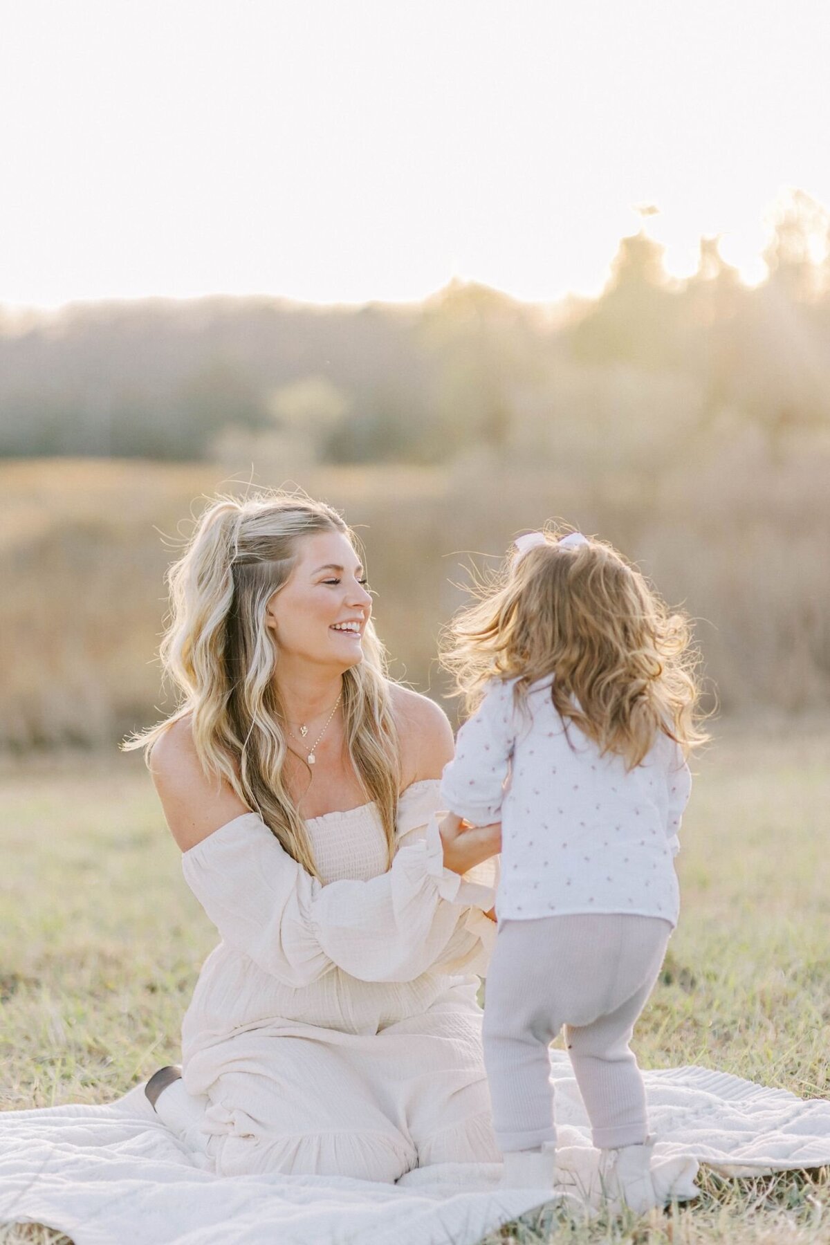 Mother sits on blanket playing with daughter