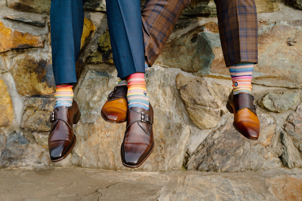 A close up view of two people's feet with dress shoes and funky socks.