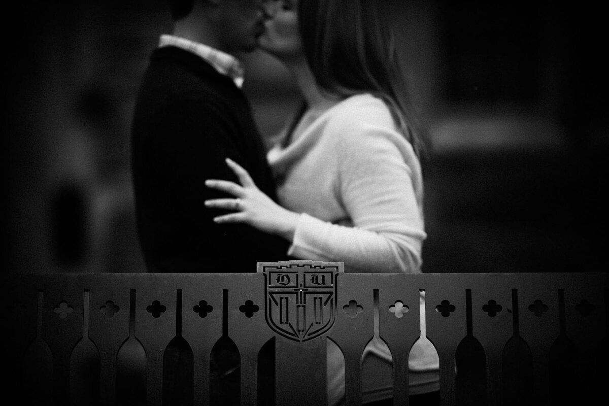 Black and white image of a couple kissing behind an ornate fence with a crest
