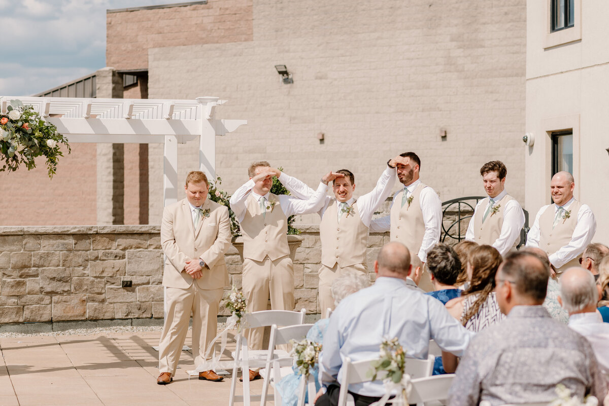 the groomsmen shield their eyes from the sun while they wait for the ceremony to begin