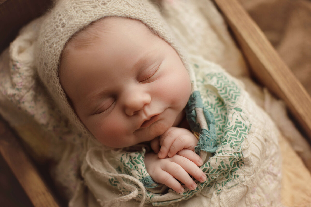 newborn baby with cream bonnet sleeping in cradle with cream quilt