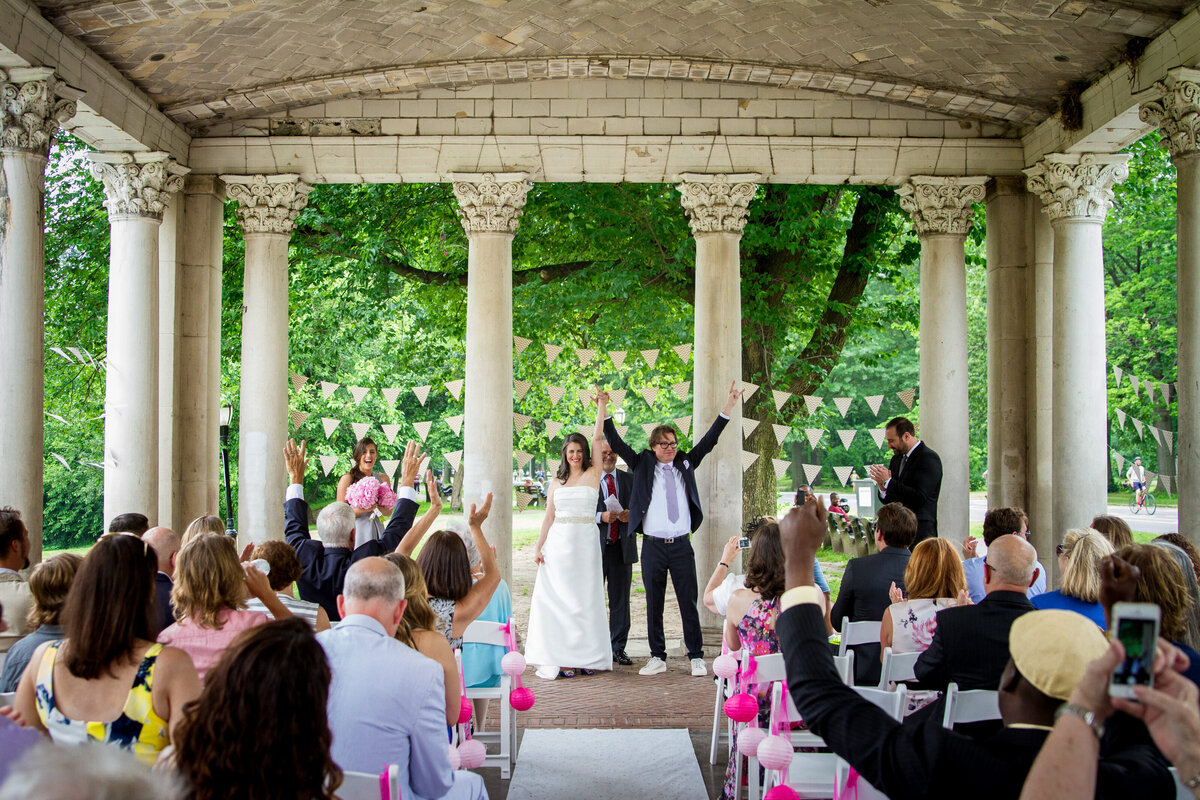 A couple holding their hands up after getting married in front of their guests.