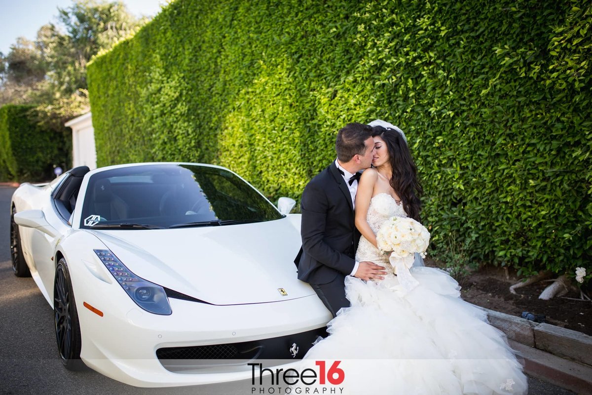 Anticipated kiss between Bride and Groom leaning up against a white car