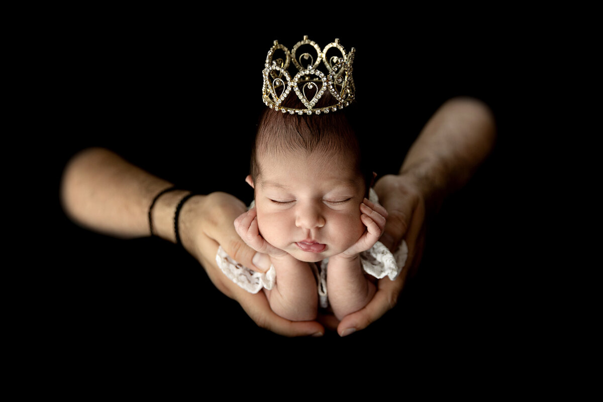 A father holds his sleeping newborn daughter as she wears a tiny crown