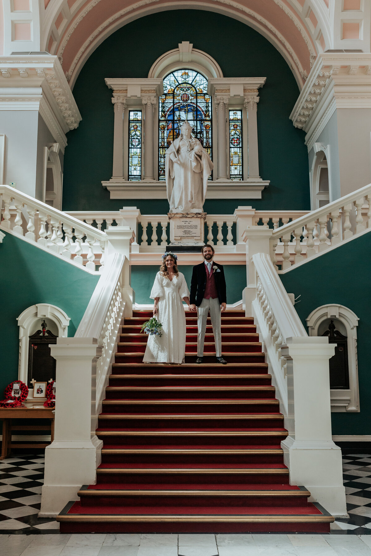 Bride and groom stand holding hands on the stairs of Woolwich Registry Office