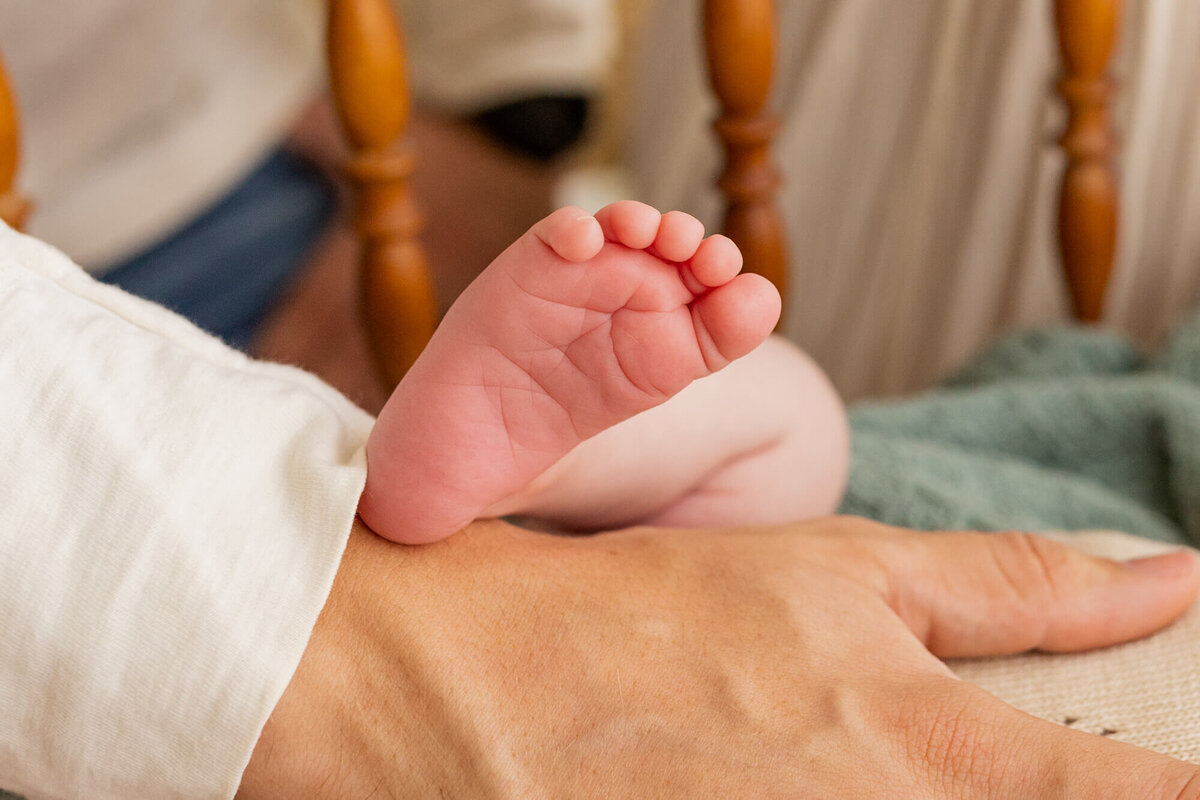 Newborn baby girl's foot propped up on her daddy's hand