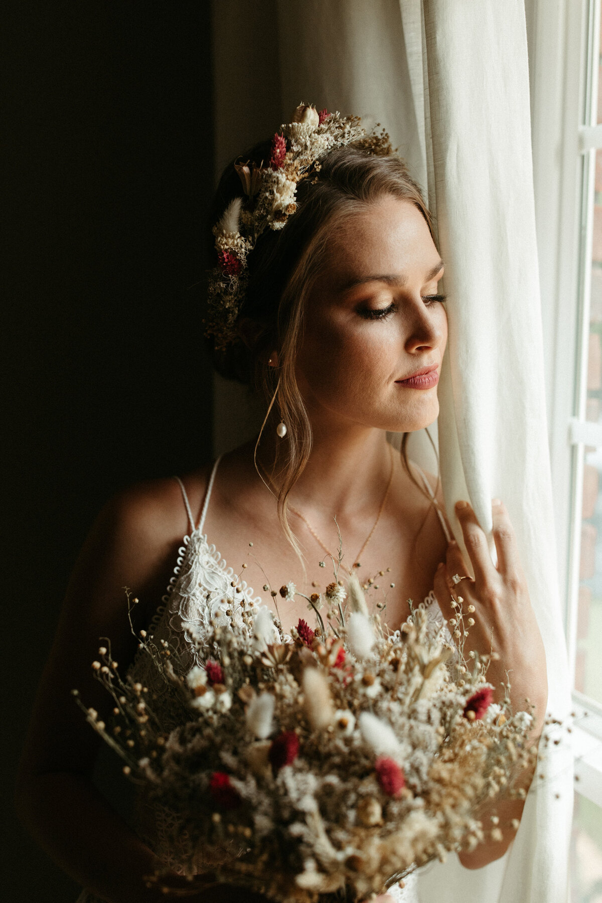 Boho bride in intricate lace dress and flower crown holding bouquet made of dried florals