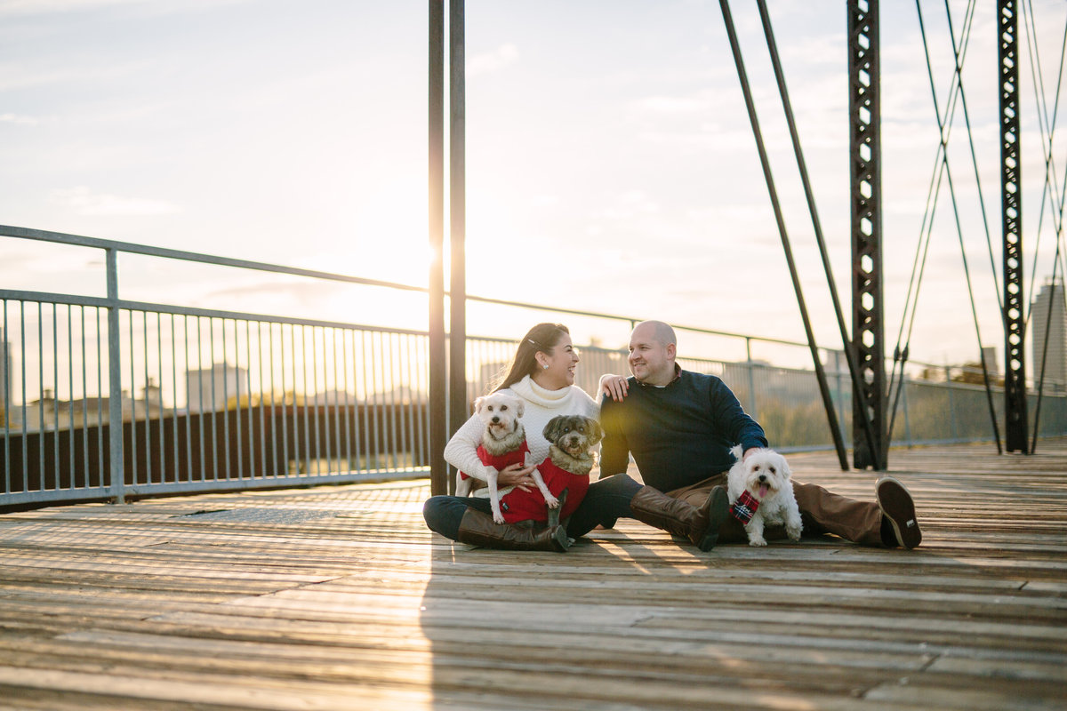 Fiancé and fiancée with their dogs sitting on a bridge in downtown San Antonio at their engagement session.