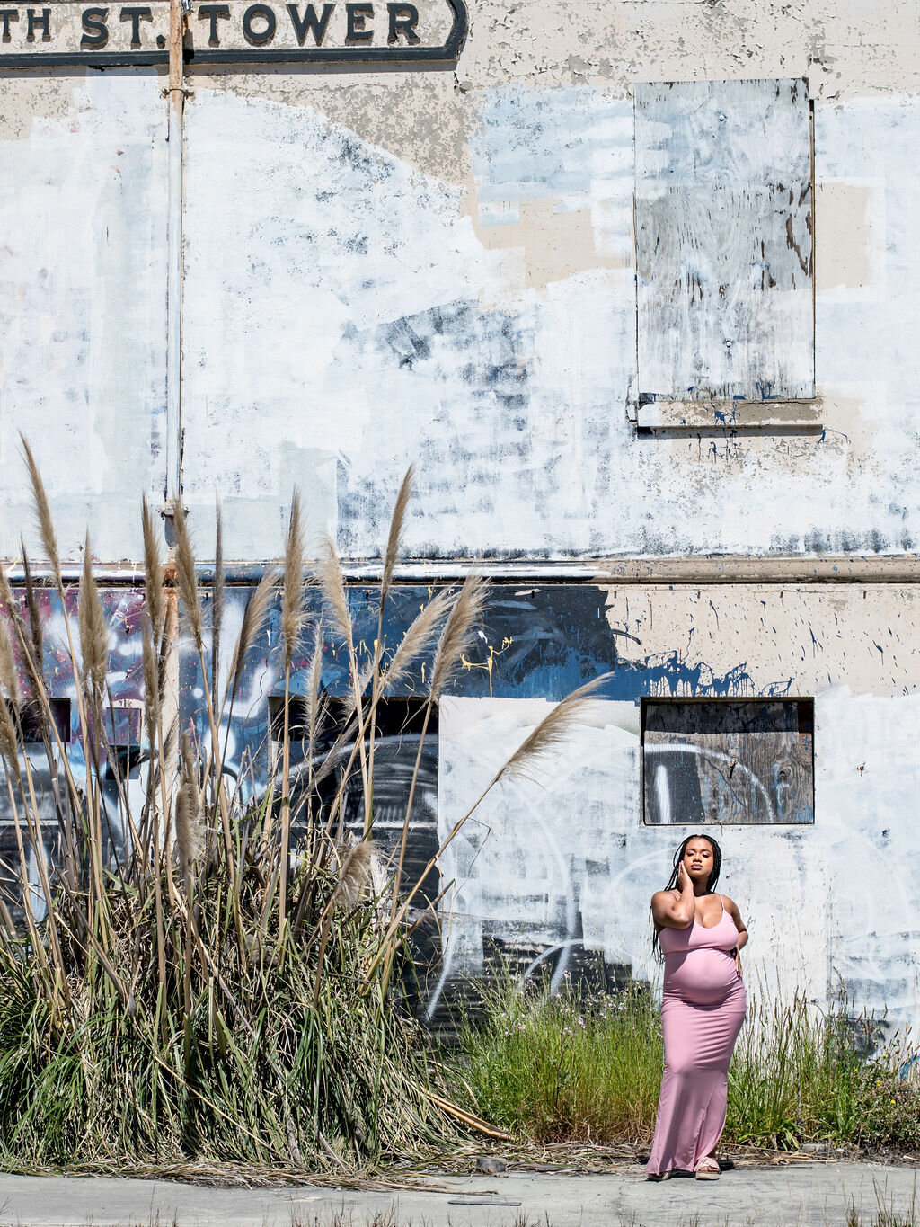 Maternity shoot of woman in pink dress in front of abandoned building in Oakland, CA