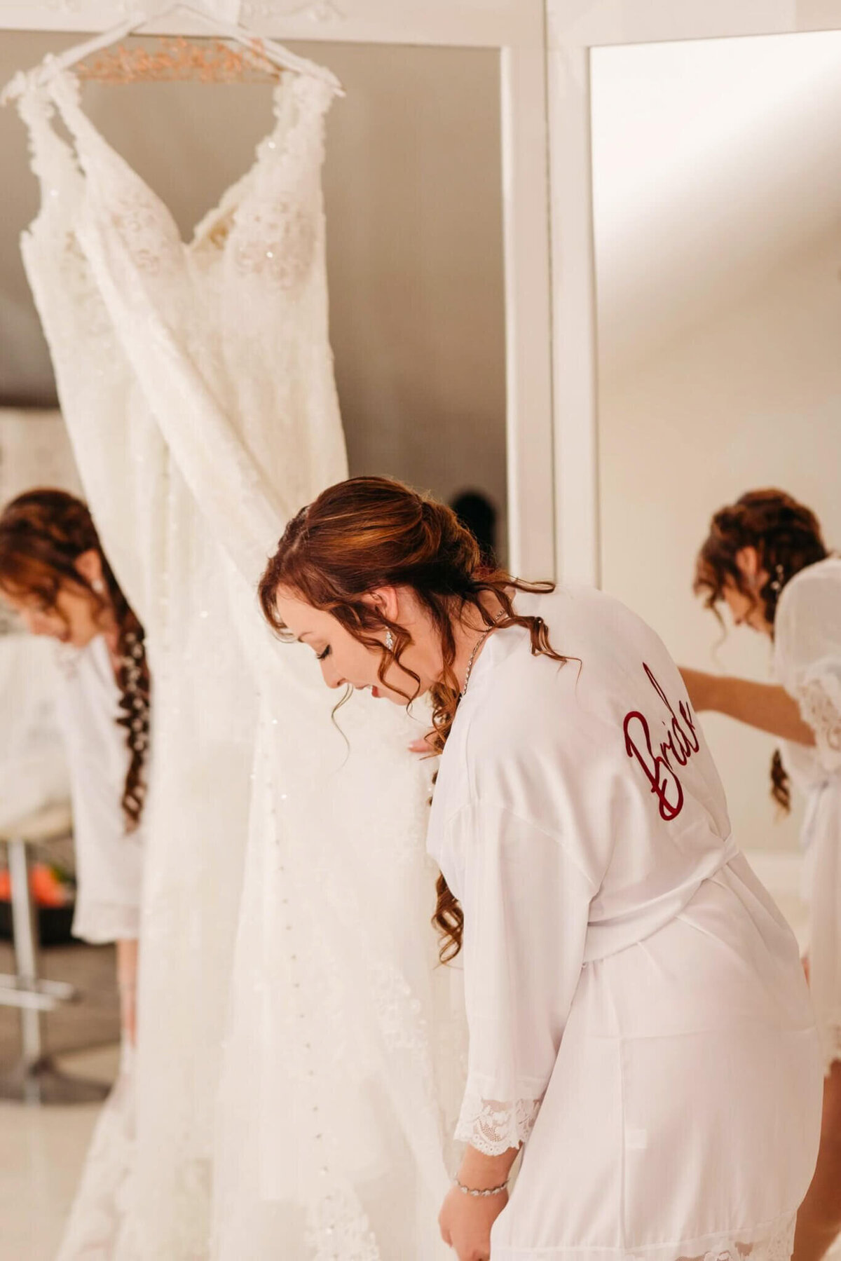A photo of a bride and a white robe holding her wedding gown