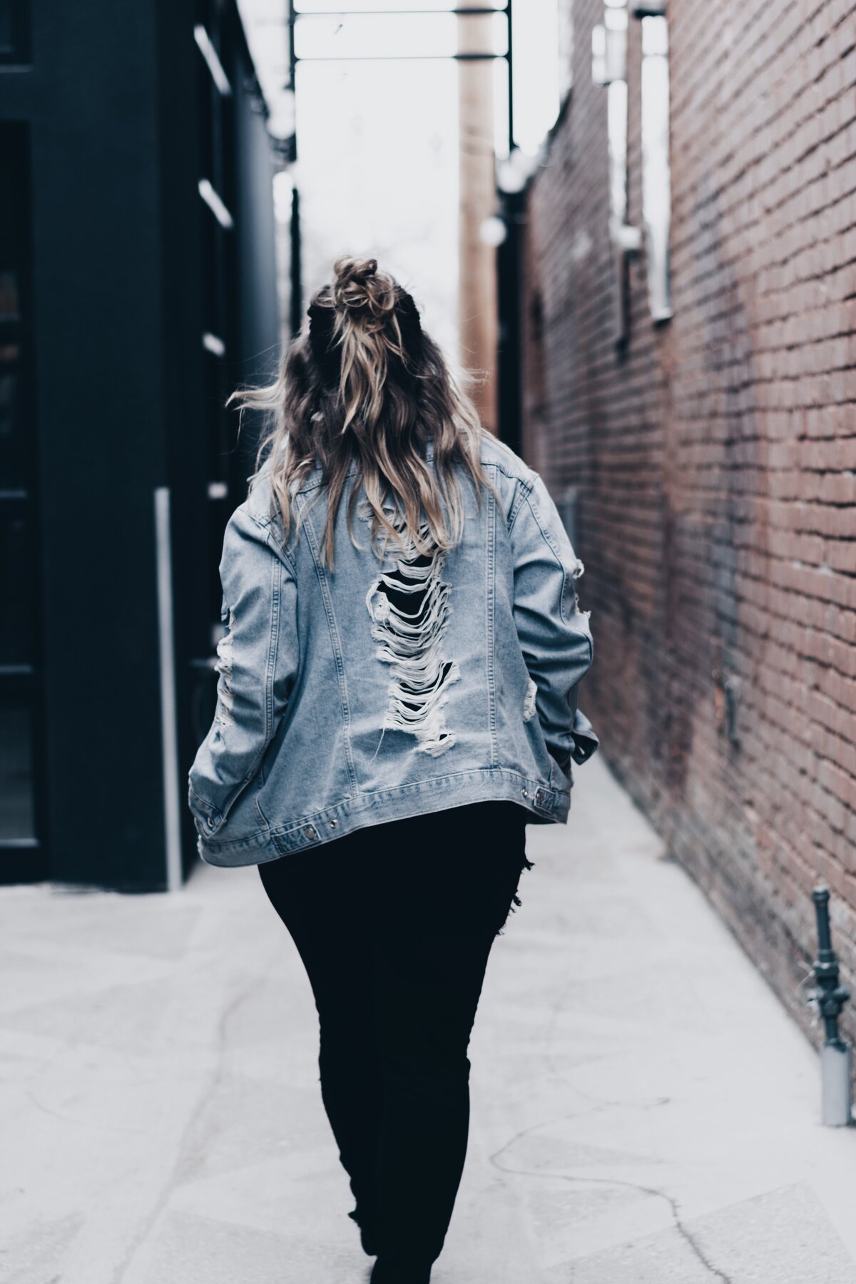 Photo of a  woman in distressed jean jacket walking away  in back alley photo.