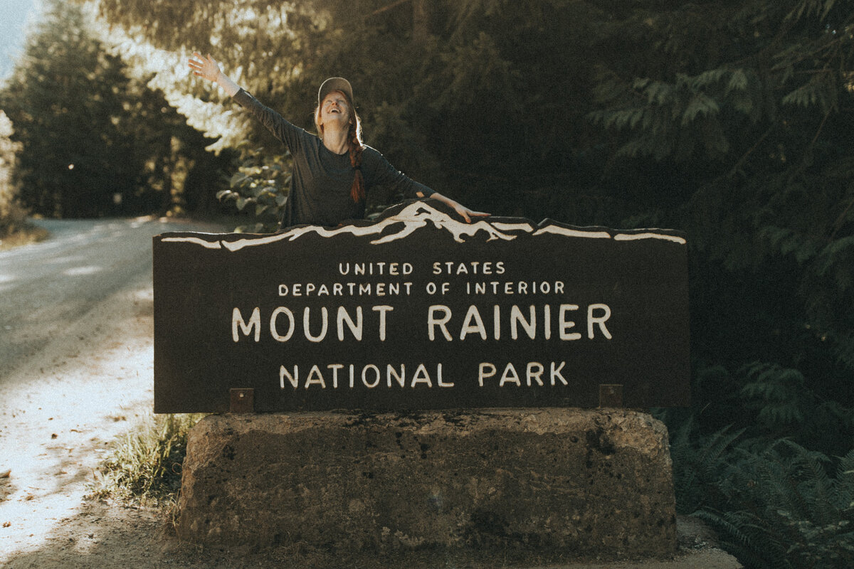 women sitting in front of mt. rainier national park sign