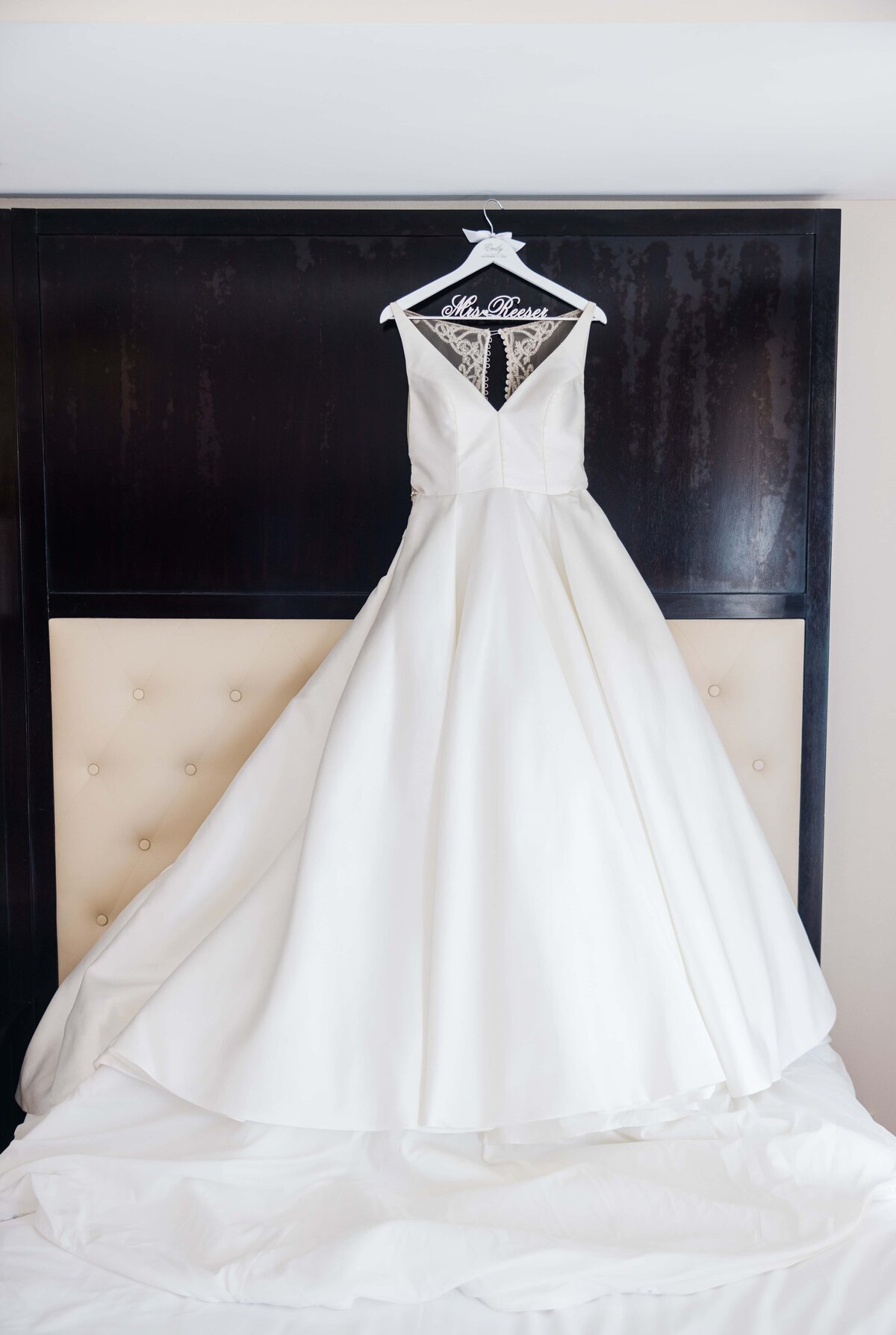 A white wedding dress hanging on a dark wooden door at a farm winery, featuring an embroidered bodice and a voluminous skirt.