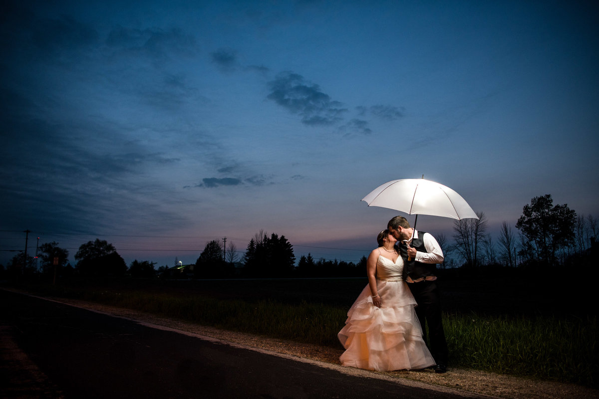 Bride and groom kiss on the side of the road in the night.