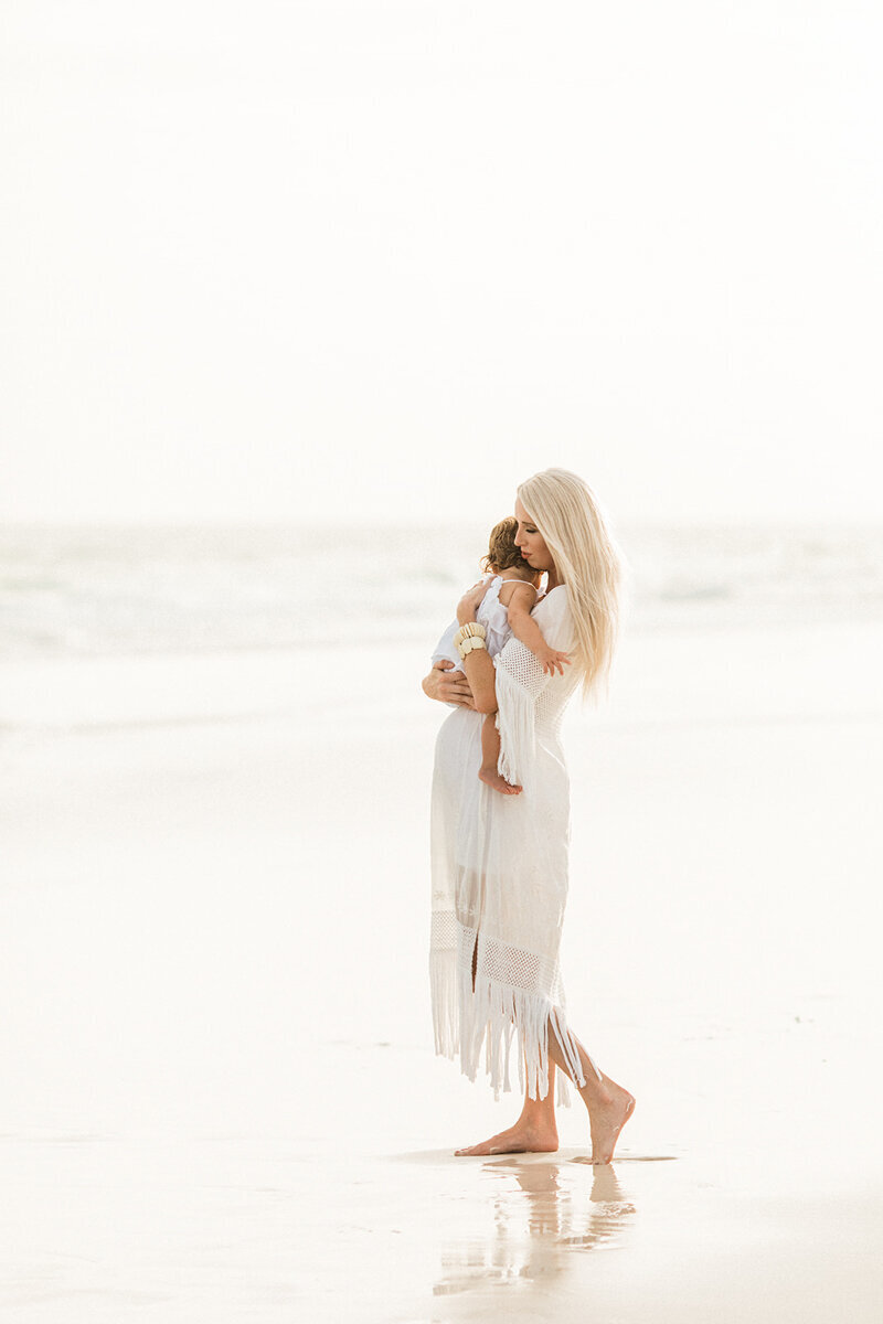 Pregnant mom walks on beach holding her toddler