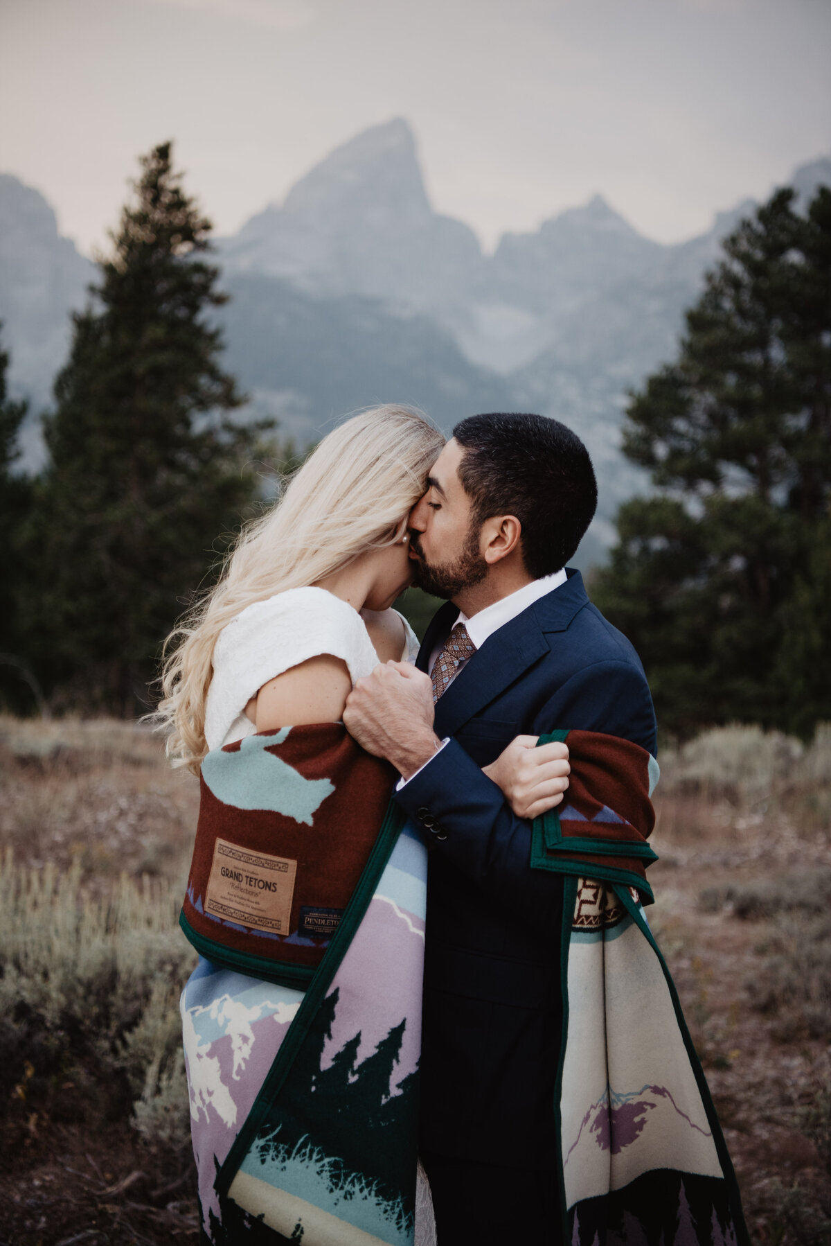 Photographers Jackson Hole capture bride and groom wrapped in blanket kissing