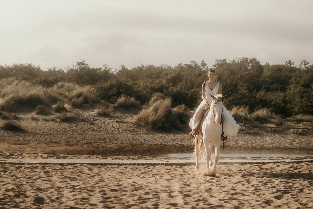 Die Braut reitet auf ihrem Pferd über den Strand gerade auf die Kamera zu.
