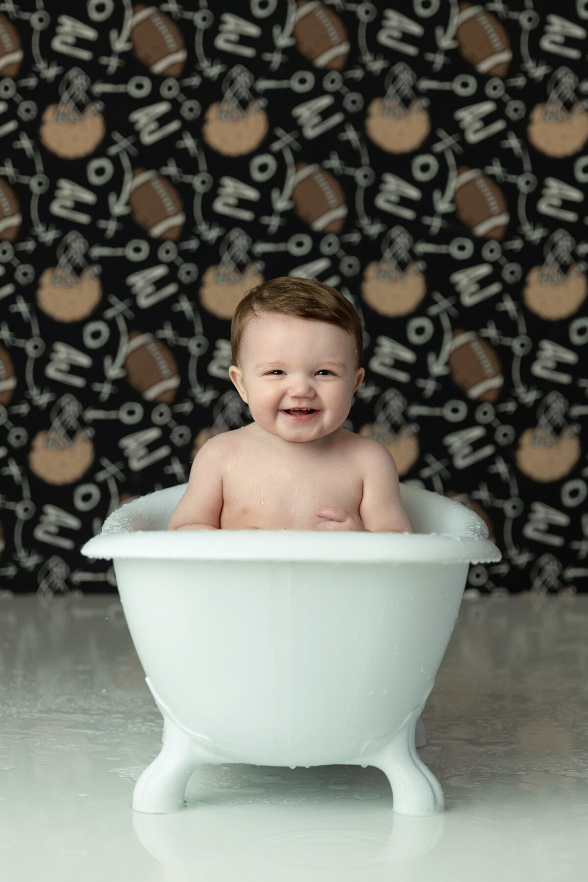 A young toddler boy sits in a small white bathtub in a studio after getting covered in cake