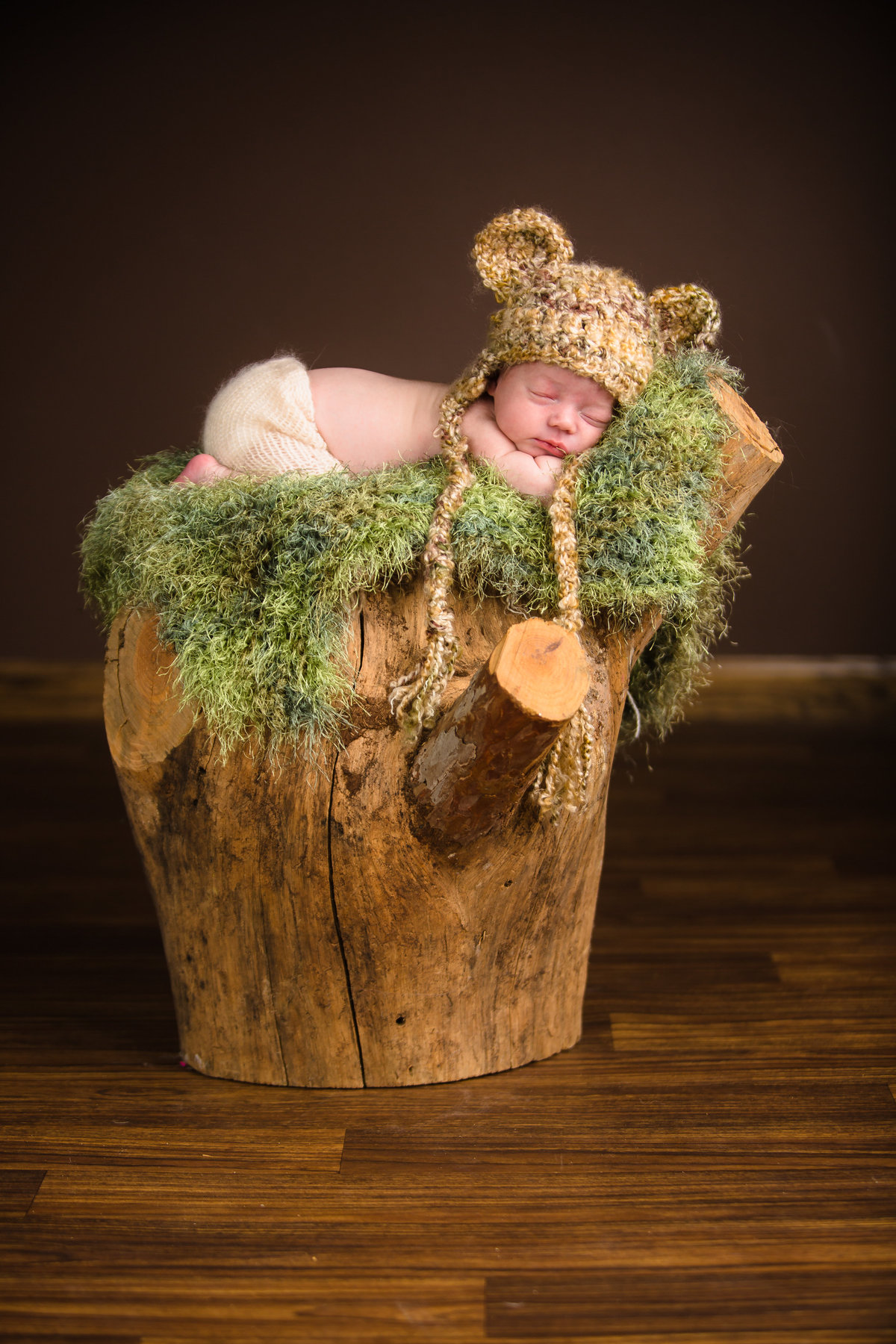 Newborn baby with a bear hat sleeping on stump