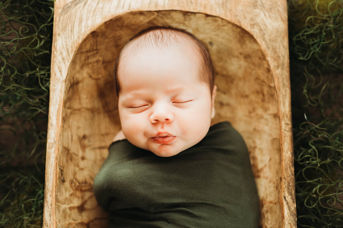 newborn baby boy wrapped in olive wrap sleeping in dough bowl.