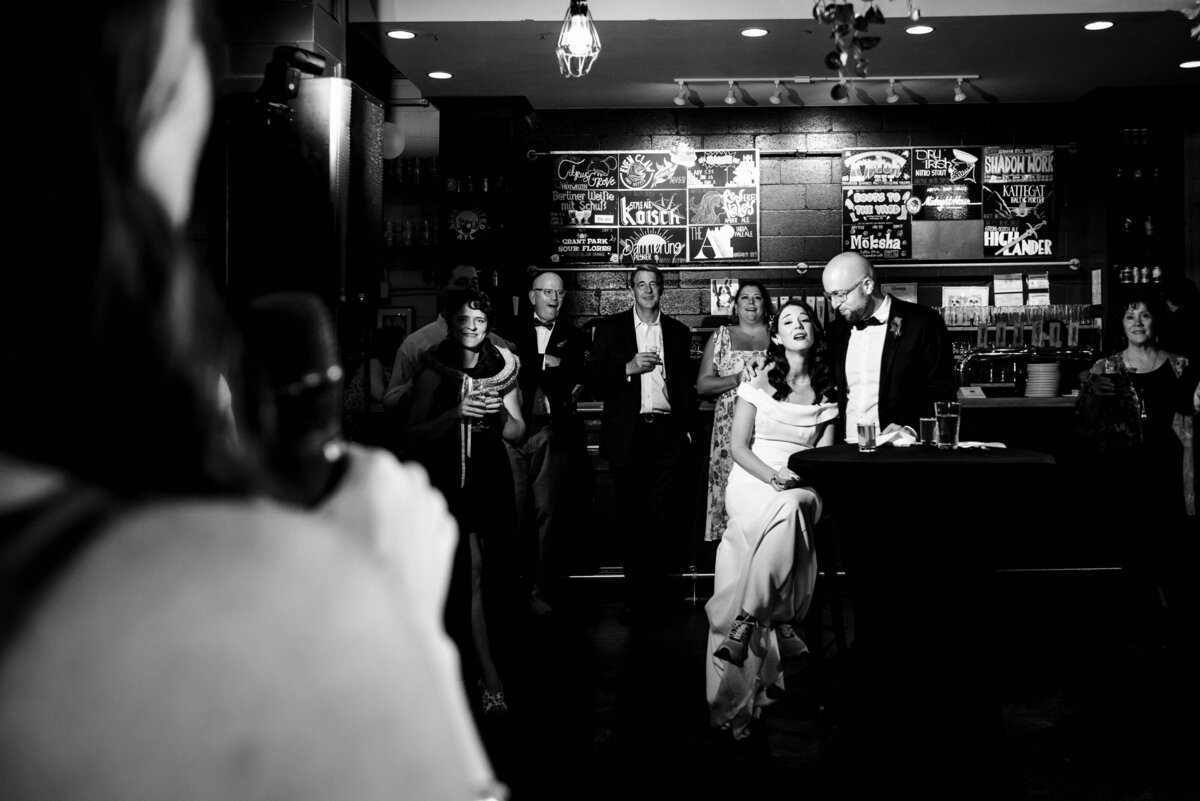 Black-and-white-photograph-of-a-bride-reacting-with-surprise-to-sister's-wedding-toast-at-Eventide-Brewing-in-Atlanta
