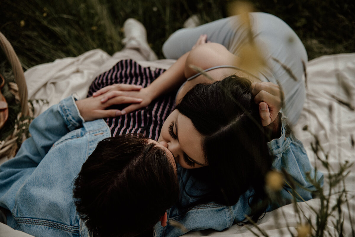 couple laying on a blanket in a field kissing.