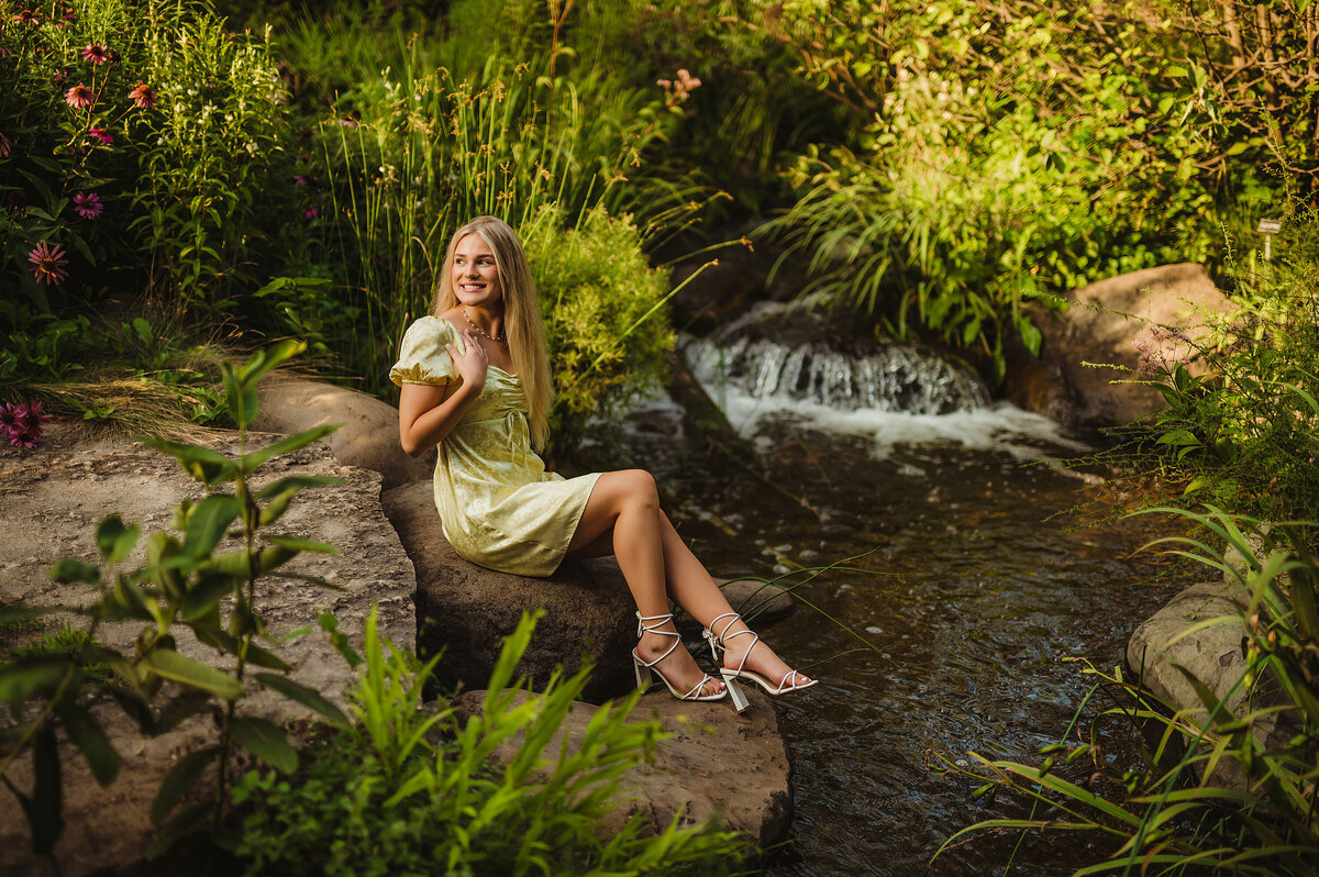 A girl from New Berlin West High School sits on rock along a stream through Boerner Botanical Gardens in Hales Corners for her senior photoshoot.