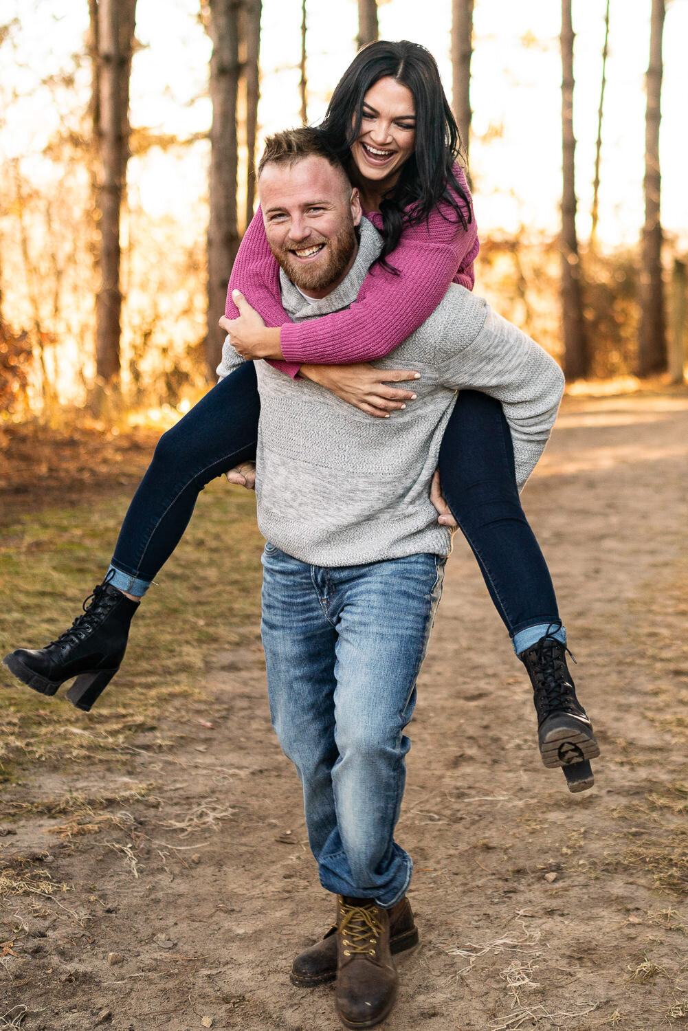 Man carries woman in pink shirt and jeans on his back.