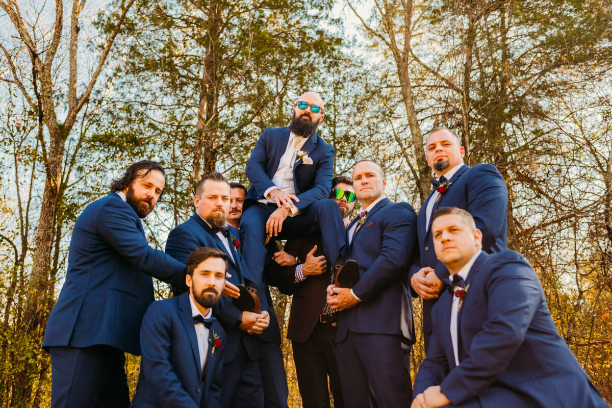 Photo of a groom sitting on his groomsmen's shoulders with a pair of sunglasses on