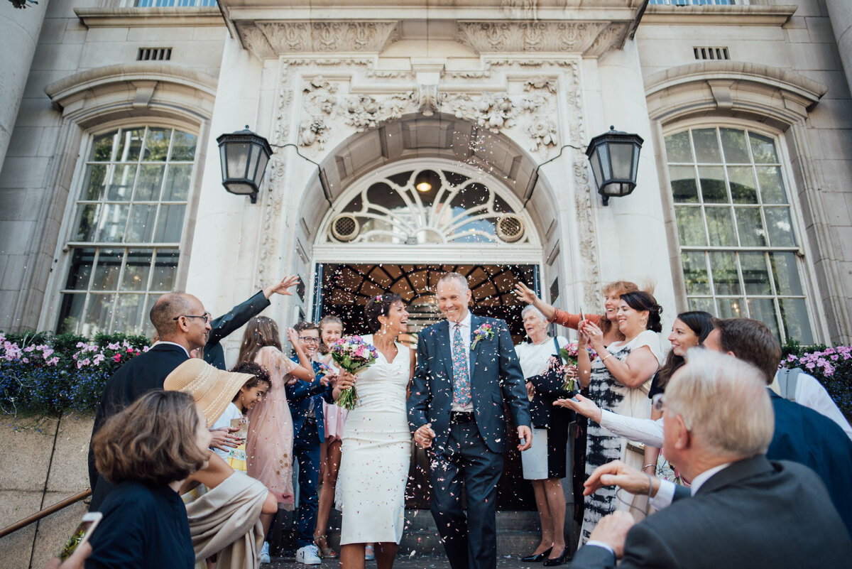 A couple walking down a staircase whilst their wedding guests throw confetti over them taken by London Wedding Photographer Liberty Pearl