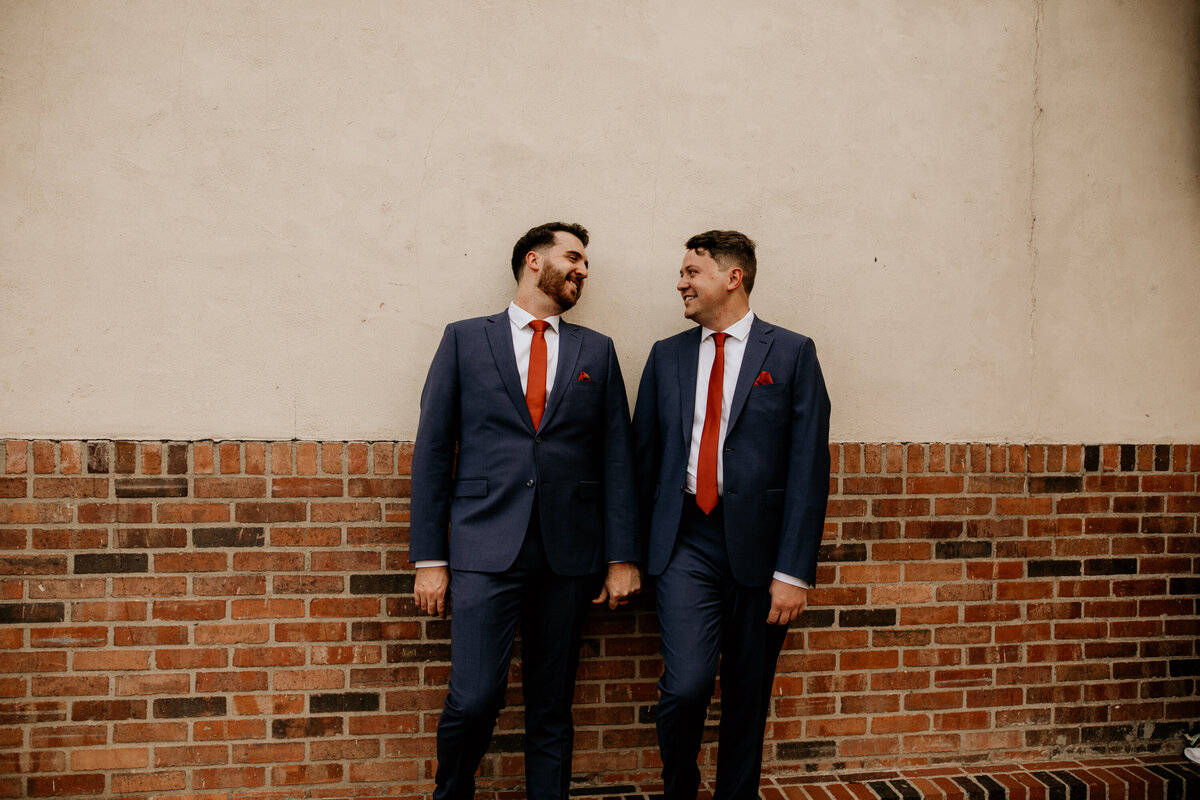 two grooms standing against a building holding hands in downtown Albuquerque