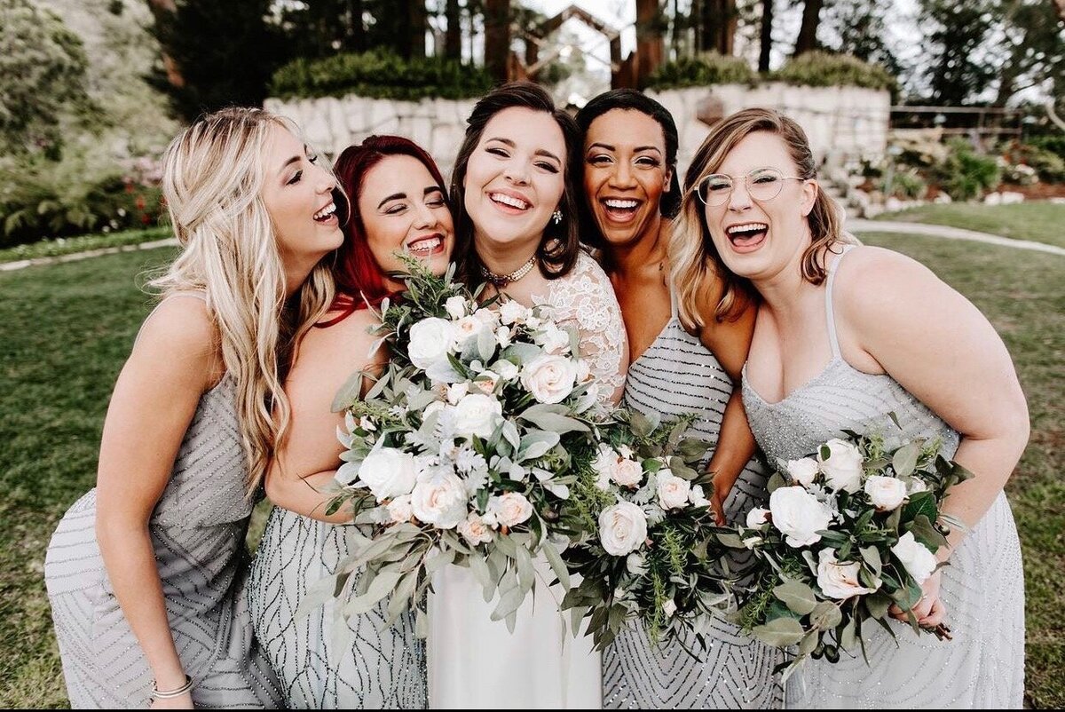 A bride and bridesmaids stand close together holding flower bouquets.