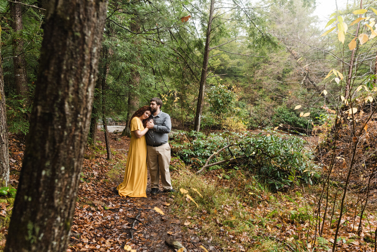 bride in mustard dress hugs groom romantically in woods at swallow falls state park