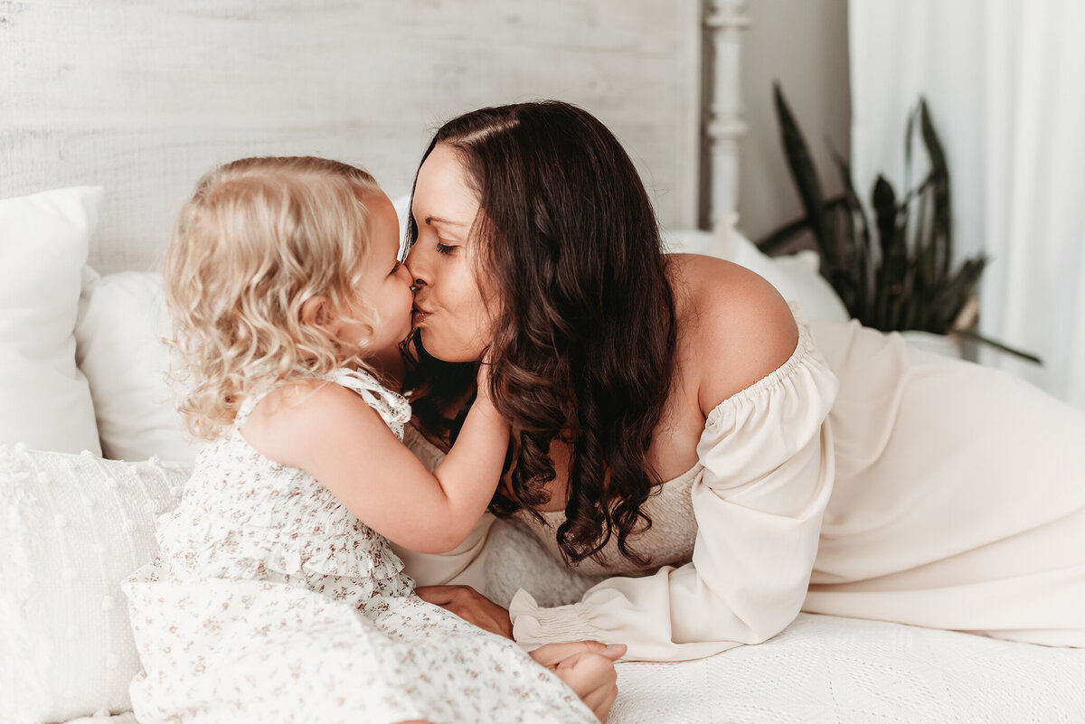 little girl kissing mom with her hands on mom's cheeks