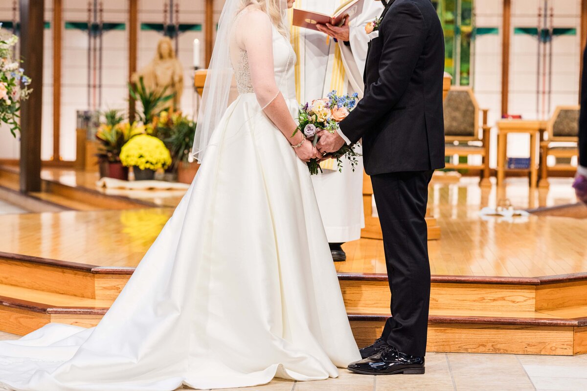 Bride and groom holding hands during a wedding ceremony at a church altar, coordinated by a top wedding planner from Des Moines, with the focus on their clasped hands and wedding attire.