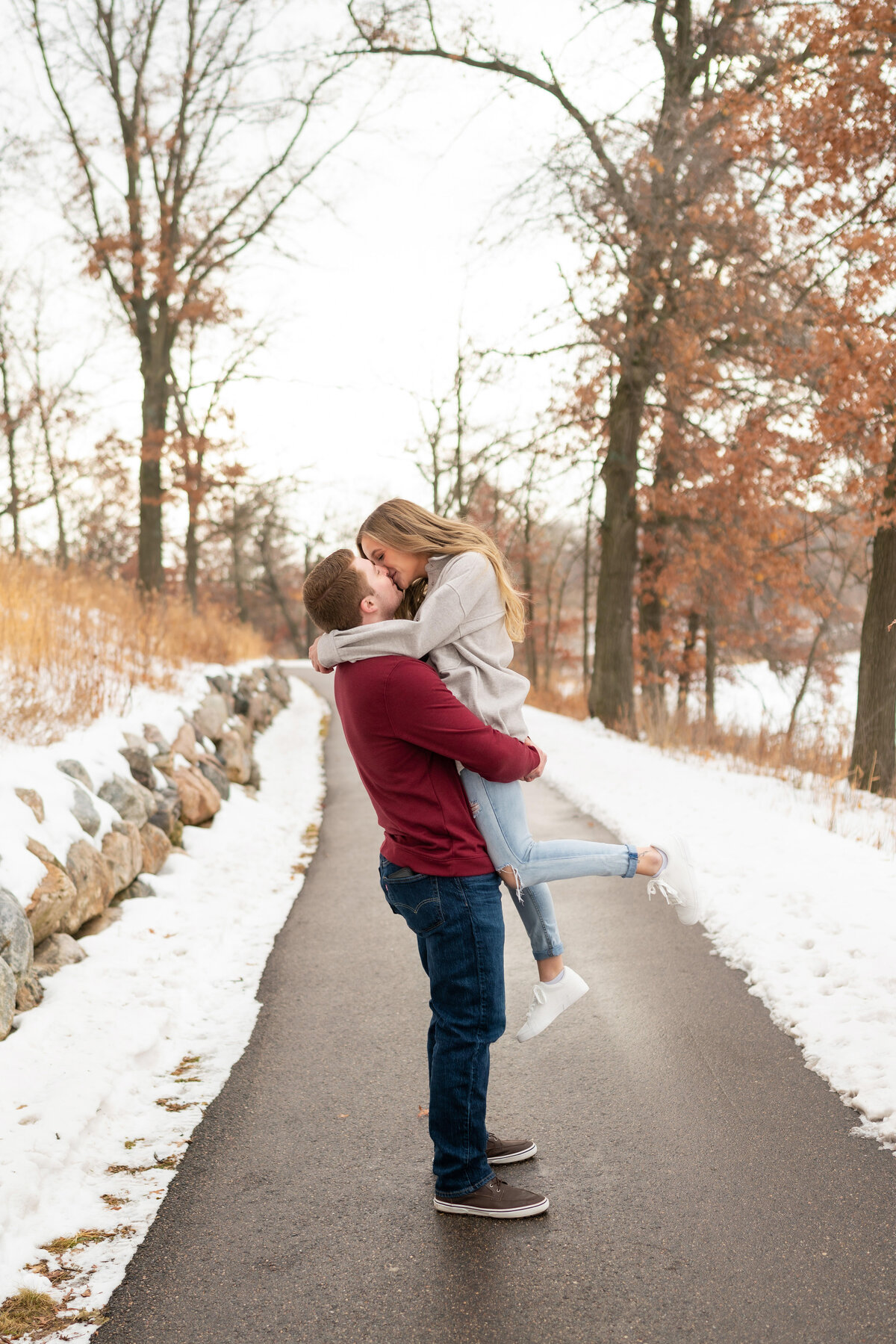 Man in jeans lifts woman in white sweater and kisses her surrounded by snow.