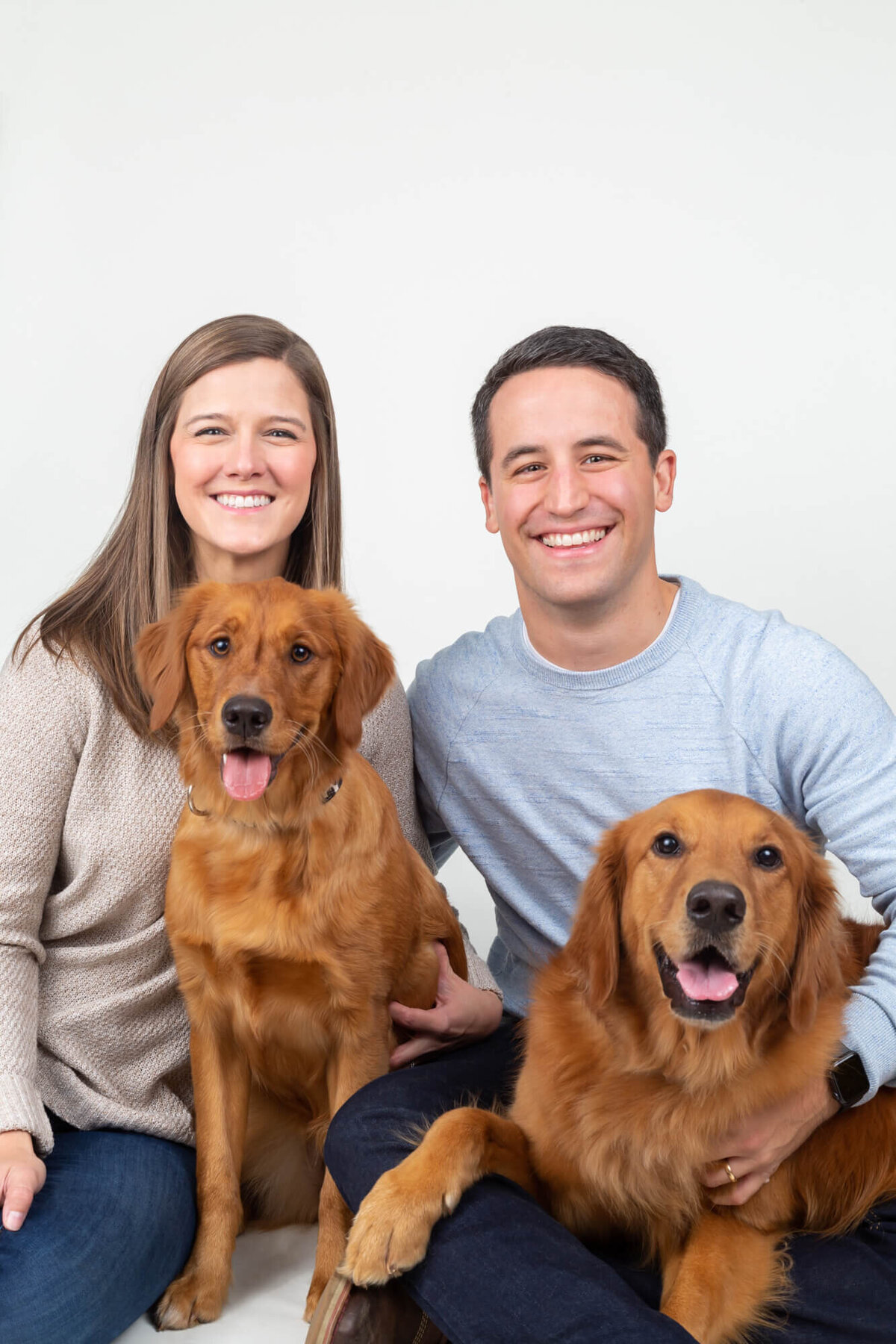 White couple with two red golden retrievers on white backdrop