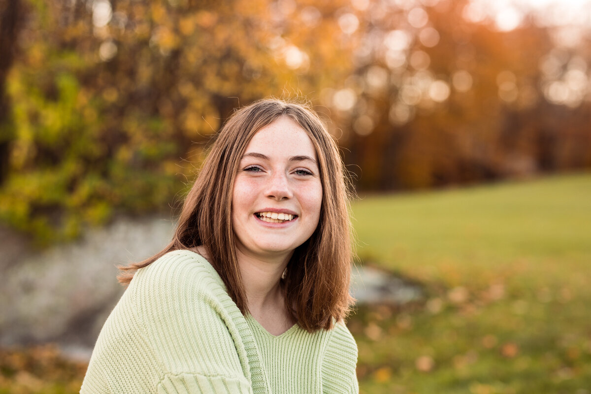 A teen girl smiles in front of fall foliage Vermont Senior Portraits