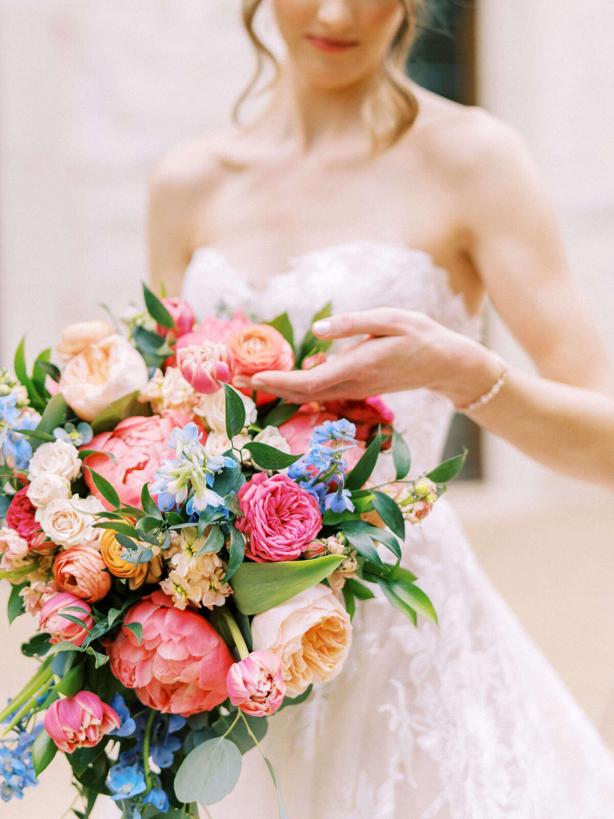 Bride wearing Monique Lhuillier gown stops to admire her colorful bridal bouquet
