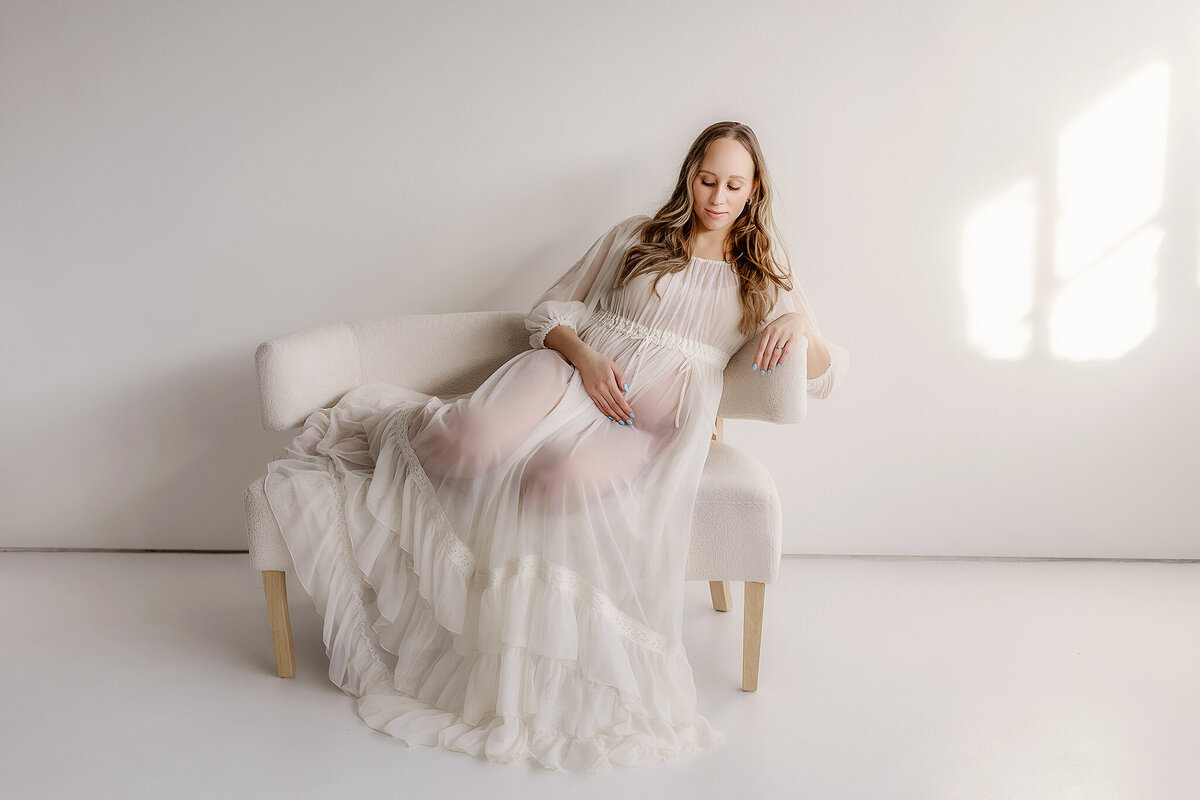 pregnant mom laying on couch in a white gown for her maternity photos in denver colorado