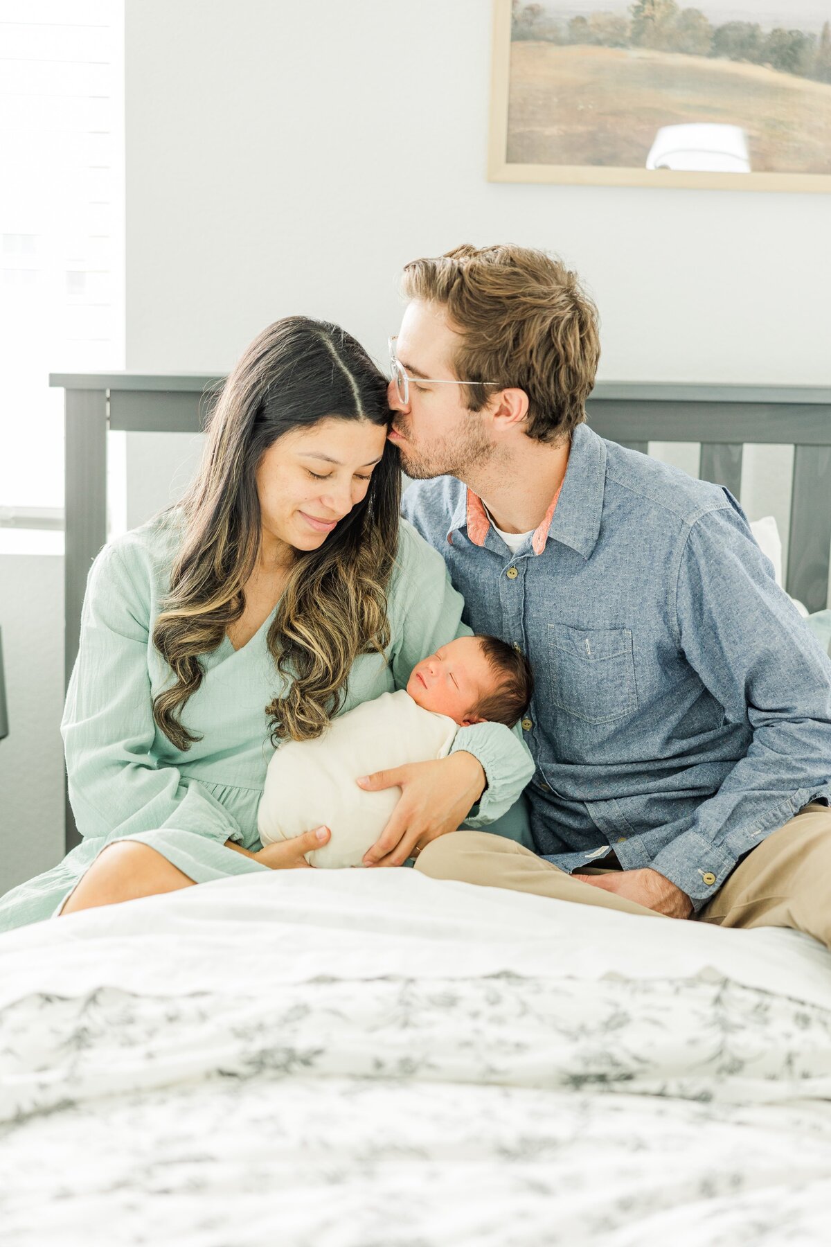 dad kisses wife while snuggling on bed for in-home newborn session