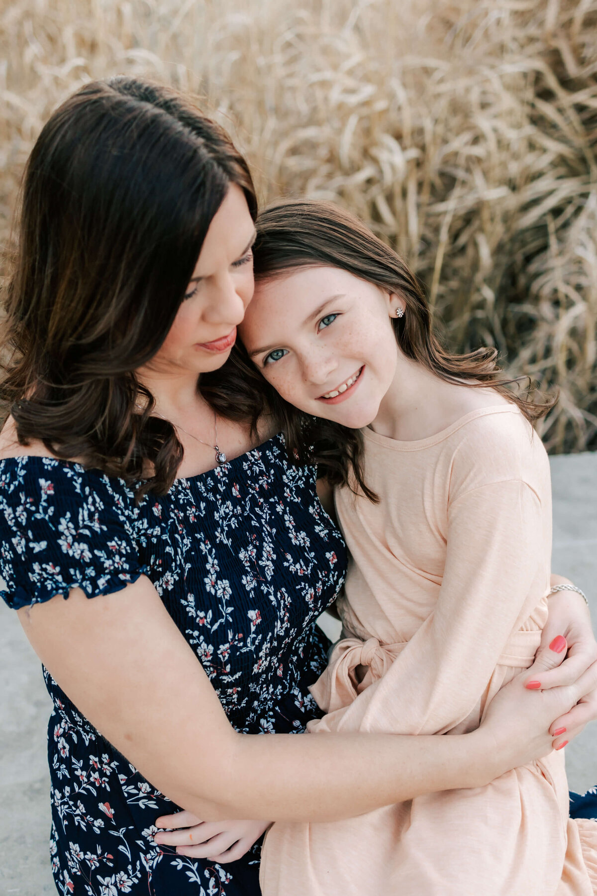a young brown haired girl sitting in her mom's lap looking up at the camera and mom has her eyes closed snuggled into her daughter