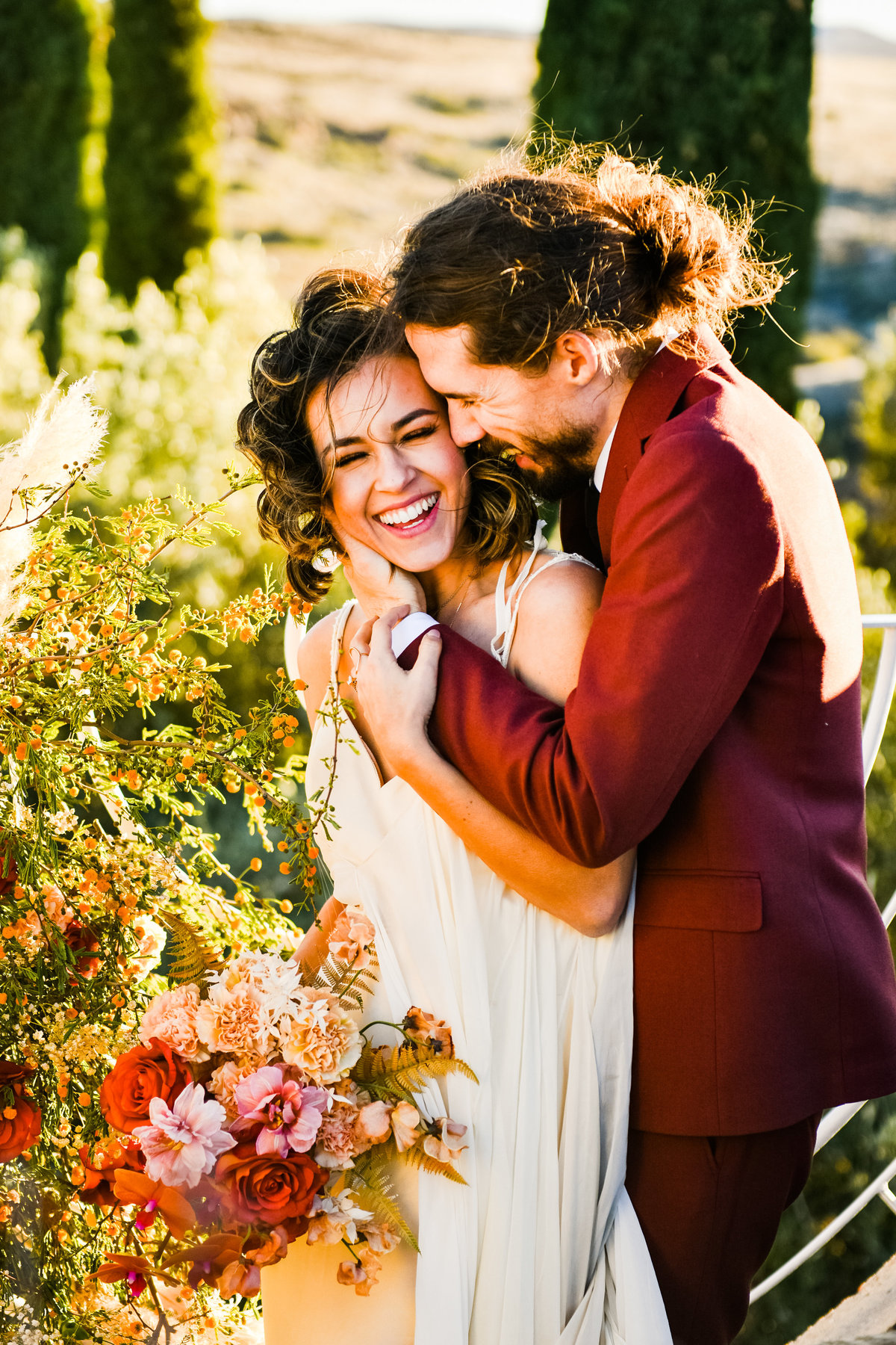 Groom holding bride floral bouquet red suit Arcosanti wedding
