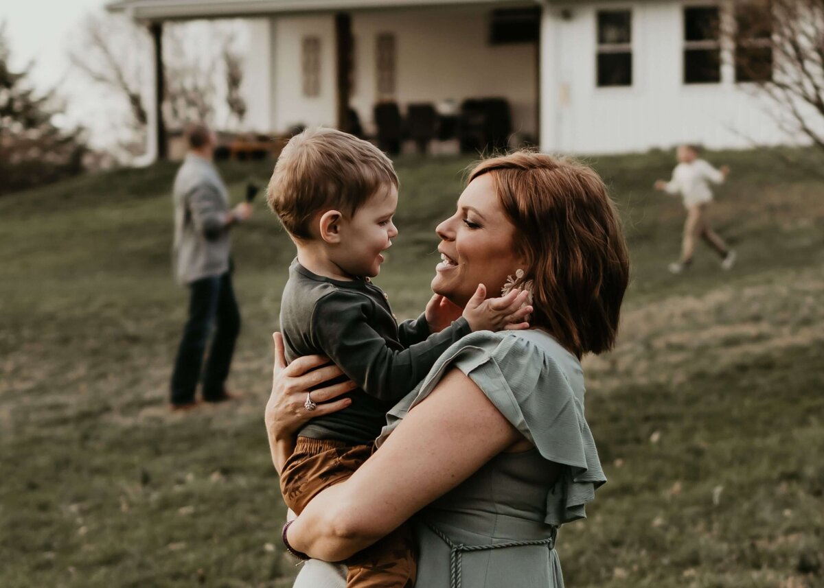 A woman holding her son in front of a house, captured by a Pittsburgh maternity photographer.