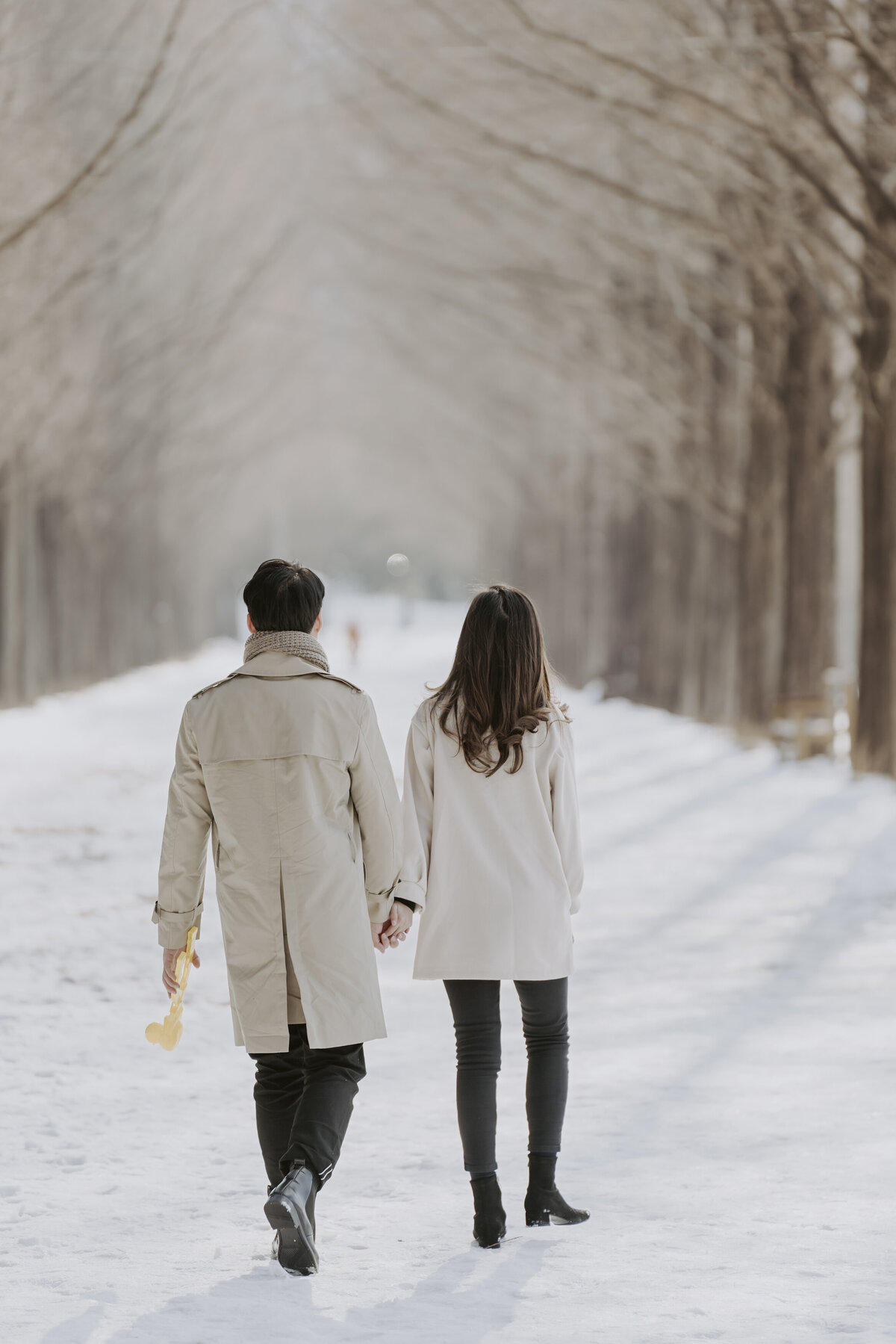 the couple hold hands while walking on a snow road in damyang