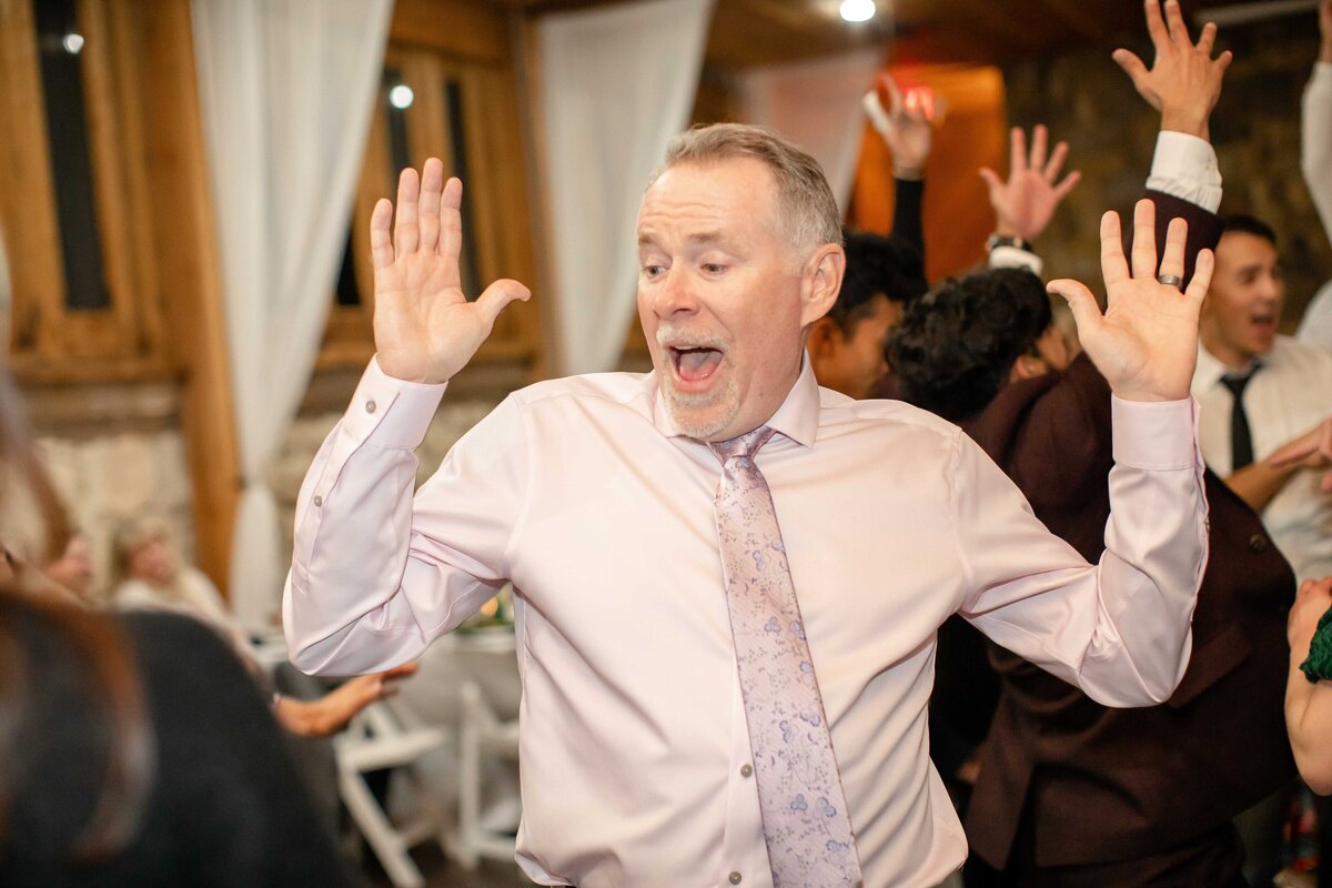 man in pink tie dances with arms raised at Fort Worth wedding