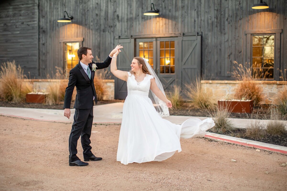 groom spins bride at Morgan Creek Barn wedding at sunset farmhouse lights shine